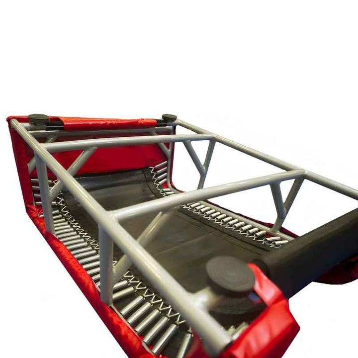 Underside of the Tumbl Trak T-Trainer showing the grey steel frame construction and rows of coiled springs along both sides, delivering the rebound that supports gymnastics vault and bar skill development