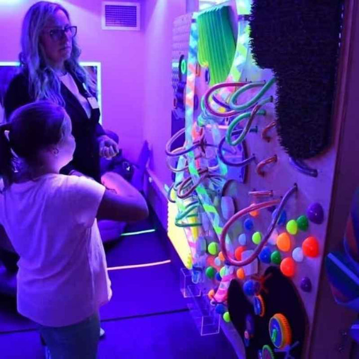 A child and caregiver exploring the TFH UV Textured Wall together under blacklight, a glowing sensory wall panel for hands-on visual and tactile play