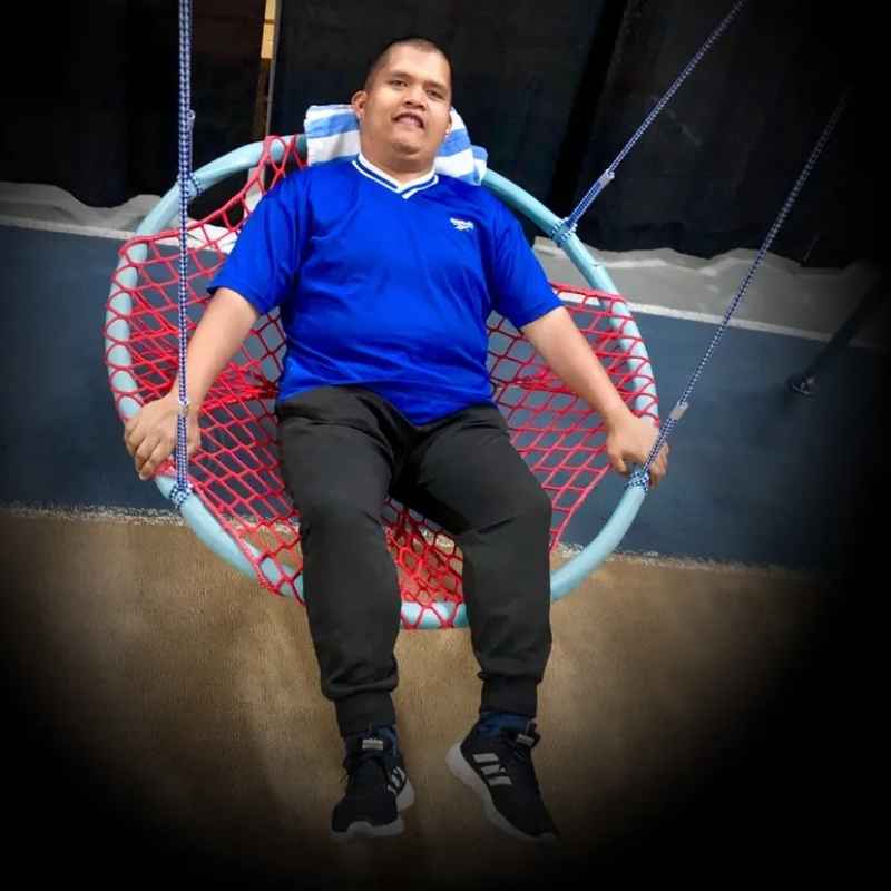 A young man using the TFH Nest Swing indoors, settled into the basket seat for calming vestibular input during therapy