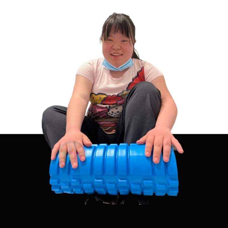 Young woman exploring the textured surface of the TFH Big Texture Vibrating Roller with both hands, a hands-on proprioceptive massage tool