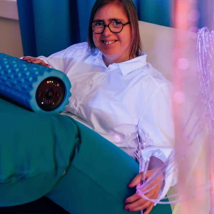 Woman relaxing in a calming sensory room while holding the TFH Big Texture Vibrating Roller, a vibrating sensory roller for deep pressure massage