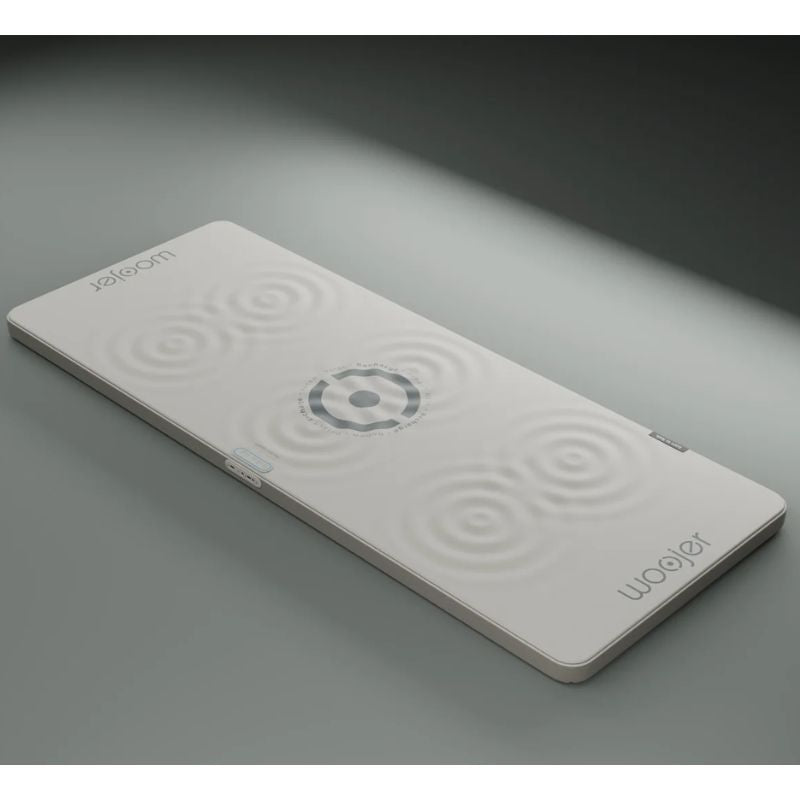 Woojer MAT Plus vibroacoustic mat in light gray with ripple graphics showing where vibration is felt, a haptic wellness mat with side controls