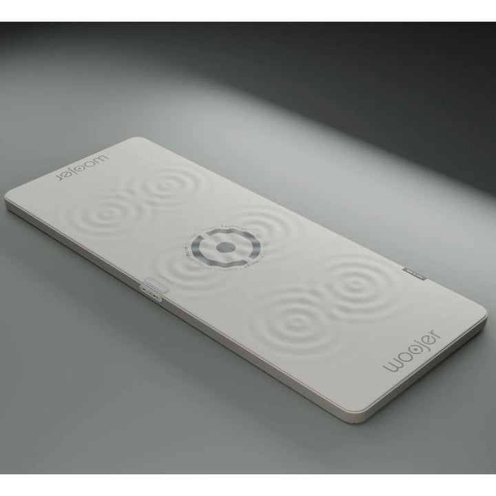 Woojer MAT Plus vibroacoustic mat in light gray with ripple graphics showing where vibration is felt, a haptic wellness mat with side controls