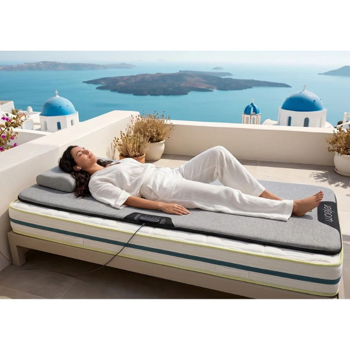 Woman lying on the Woojer MAT vibroacoustic mat on top of a mattress on a sunny rooftop terrace, unwinding with a portable vibrating mat