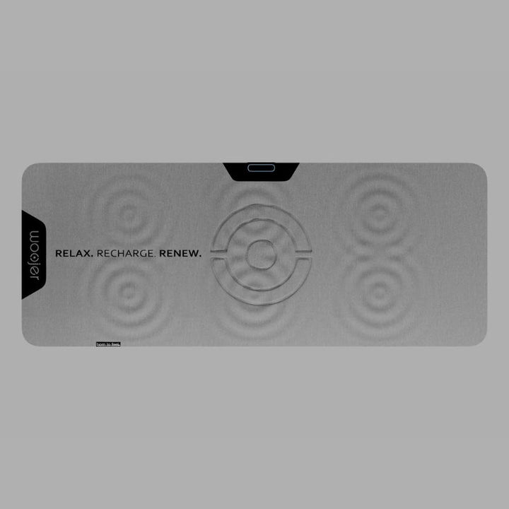 Woojer MAT vibroacoustic mat shown from above, with ripple markings across its haptic zones and a center control area on a gray vibrating mat