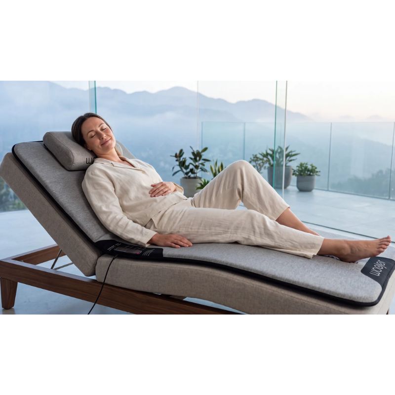 Woman resting with her eyes closed on the Woojer MAT vibroacoustic mat on a reclining lounger, enjoying full-body vibroacoustic relaxation