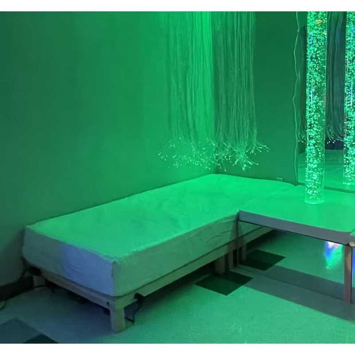 TFH Vibroacoustic Waterbed in a calming green-lit sensory room with fibre optic tassels and a bubble tube reflected in the mirror