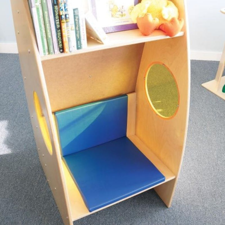 Close-up interior view of the Whitney Brothers Alone Zone showing the book storage above the seat, yellow acrylic side portal window, and the included blue padded seat cushion