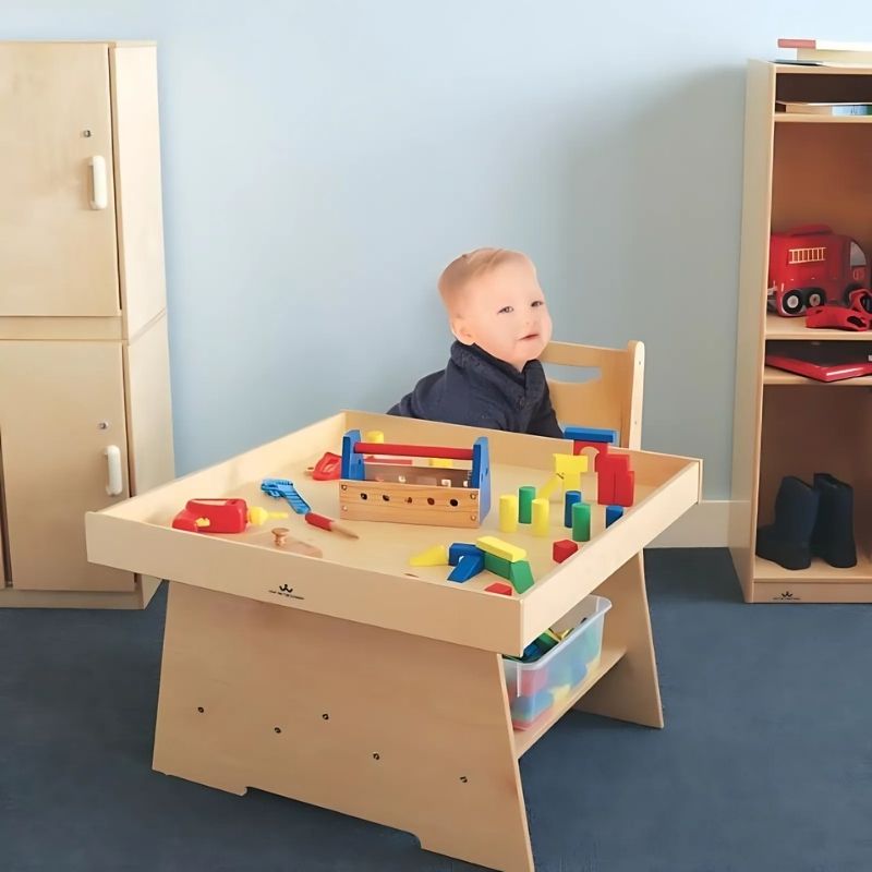Toddler playing at the Whitney Brothers Big Wide Discovery Table, showing the low 20" height, wide 31"x31" surface, and raised perimeter lip that keeps objects from falling off