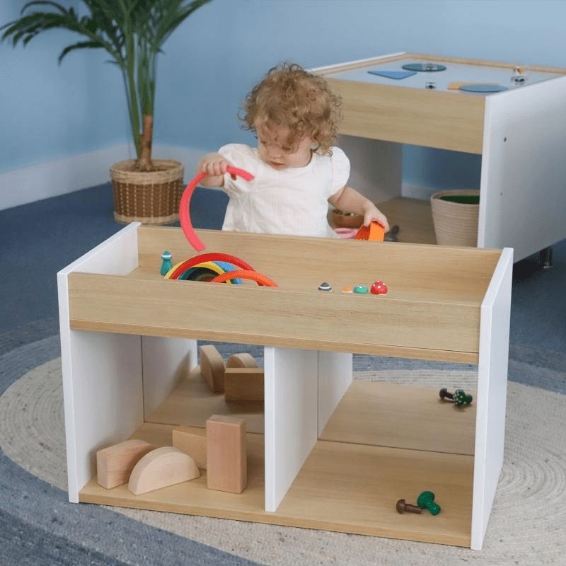 Toddler pulling up to stand at the Whitney Brothers elevatED I-See-Me Toddler Mirror Cabinet, showing the shatterproof acrylic front mirror and the toddler-height self-discovery cabinet
