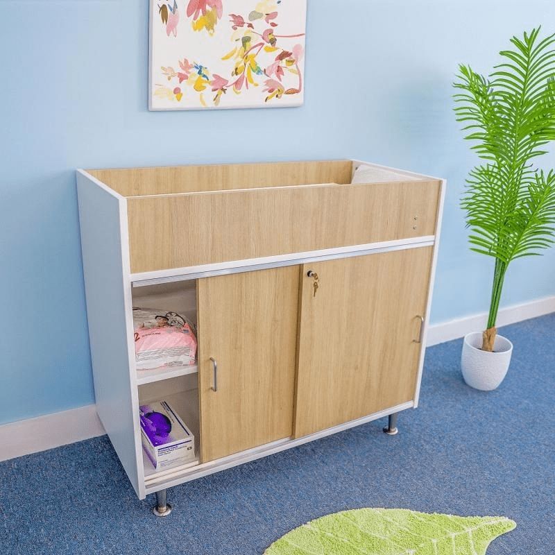 Whitney Brothers elevatED Infant Changing Cabinet in an infant room setting, showing the contemporary two-tone white panels, textured white oak, and brushed nickel legs of the changing cabinet