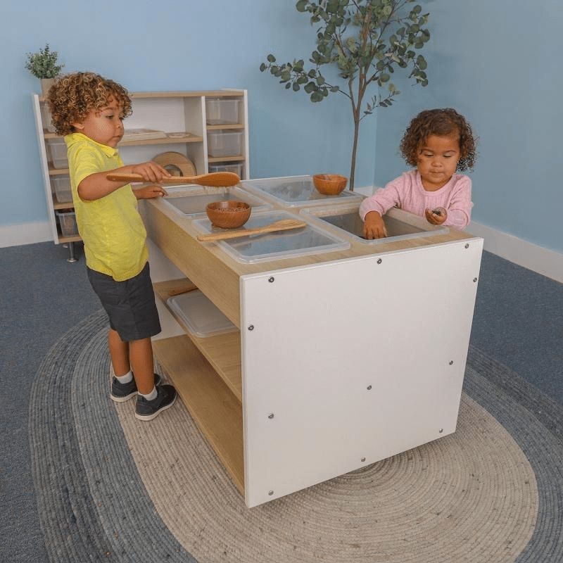 Children engaged in dry sensory play at the Whitney Brothers elevatED Mobile Sensory Table, showing the four removable trays with lids and the contemporary two-tone elevatED Collection design