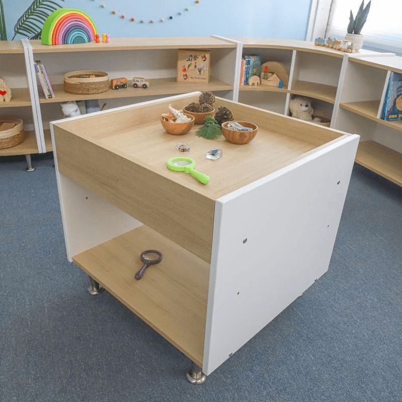 Whitney Brothers elevatED Toddler Discovery Table in a classroom setting, showing the full 26" wide contemporary two-tone activity table with ample open storage underneath