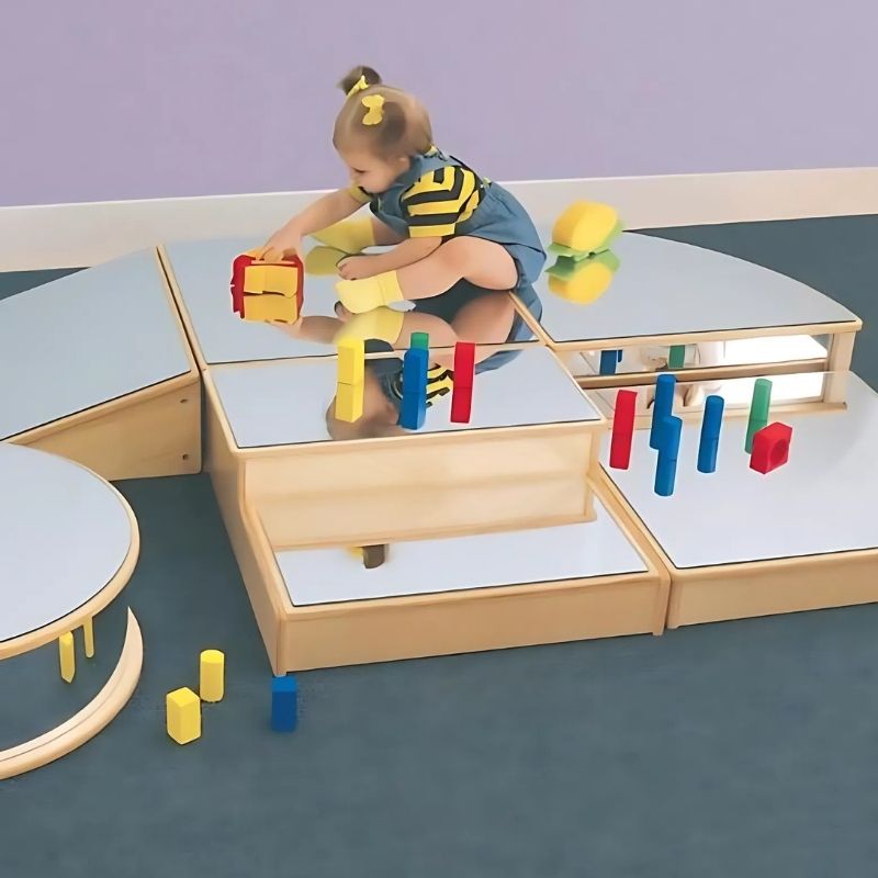 Top-down view of an infant playing with the Whitney Brothers Infant Floor Mirror Set, showing the six different shatterproof mirror blocks arranged on the floor for crawling baby exploration