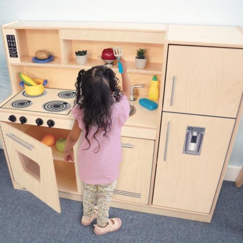 Child engaged in imaginative kitchen play with the Whitney Brothers Contemporary Kitchen Combo Natural, showing the clicking knobs and chrome faucet of the compact all-in-one play kitchen