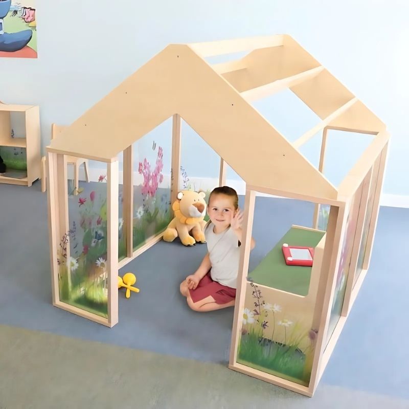 Child playing inside the Whitney Brothers Nature View Play Greenhouse, showing the wildflower-printed acrylic panels, open pergola roof, and wide door openings of the indoor classroom greenhouse