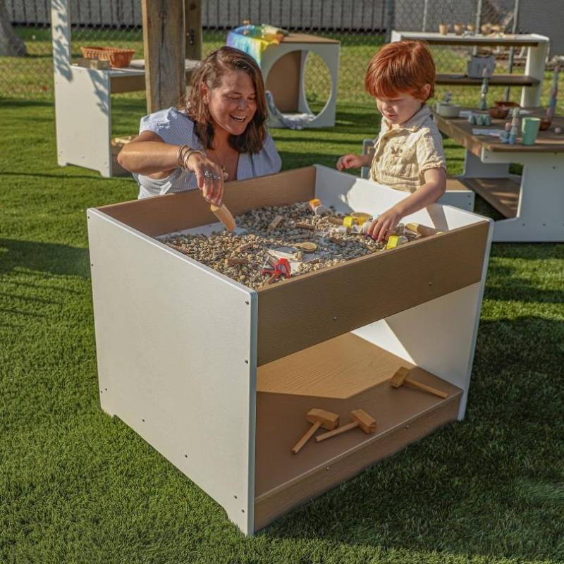 Mother and child engaged in outdoor sensory play at the Whitney Brothers outdoorED Big and Wide Table, showing wide base stability and spacious reversible-top play surface
