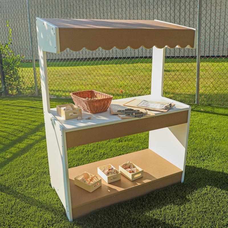 Whitney Brothers outdoorED outdoor dramatic play stand landscape view showing full sloped awning, 47.5-inch stand height, and dual-sided lower storage shelf in outdoor preschool setting