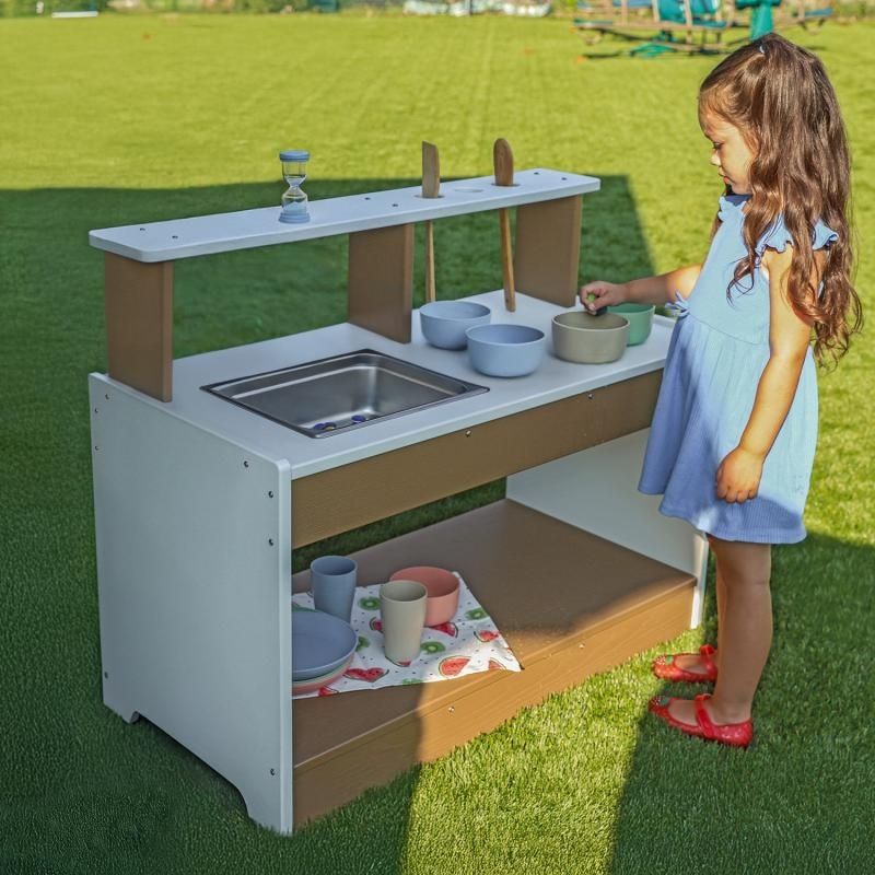 Child actively playing at the Whitney Brothers outdoorED Mud Kitchen outdoors, engaging in open-ended sensory play with water and natural materials