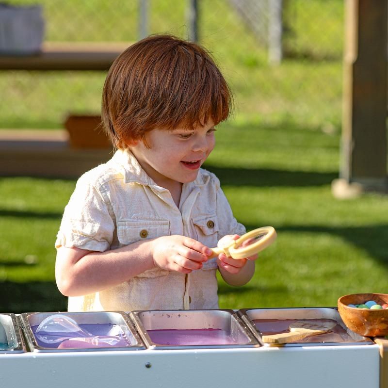 Boy engaged in outdoor potion mixing at the Whitney Brothers outdoorED Potion Station, showing extra-wide stability feet and child-scaled 24-inch working height