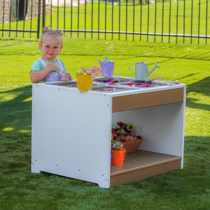 Child actively exploring tactile materials at the Whitney Brothers outdoorED Sensory Table outdoors, showing four stainless steel tray configuration in use