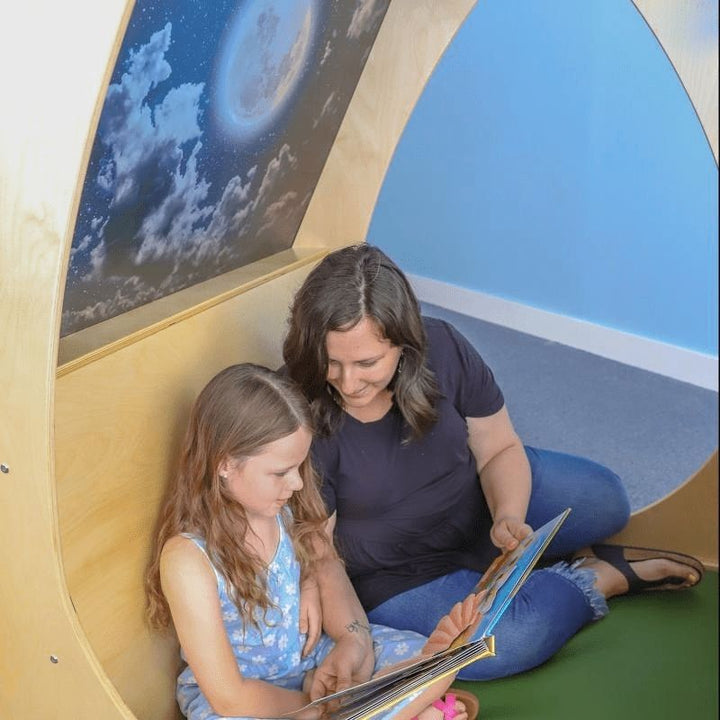 Adult and child reading together inside the Whitney Brothers Sky View Sanctuary, showing the interior floor pad, built-in backrests, and the capacity for two children and one adult