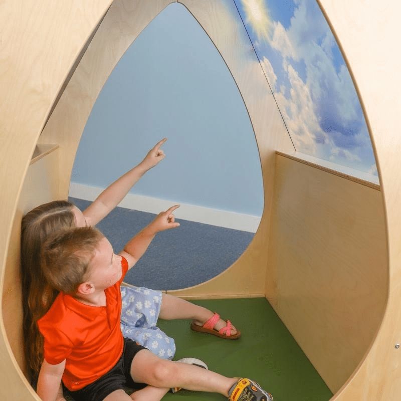 Two children inside the Whitney Brothers Sky View Sanctuary pointing up at the day sky imagery on the shatterproof acrylic panels of the biophilic quiet space classroom nook
