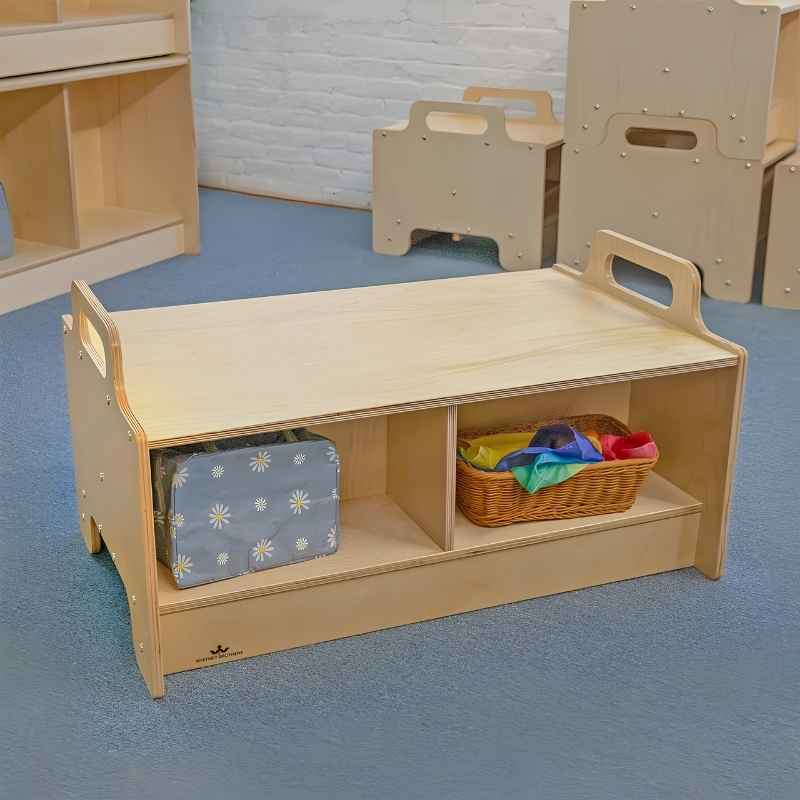 Whitney Brothers Stack-Able Bench on a classroom floor with learning materials stored in the under-seat compartments, with other Stack-Able Collection furniture pieces visible in the background