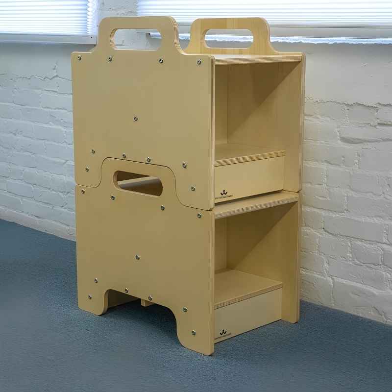 Two Whitney Brothers Stack-Able Seats stacked and configured as a two-sided storage unit in an early learning classroom, with the side hand-hold cutout visible and open compartments on both sides ready for materials