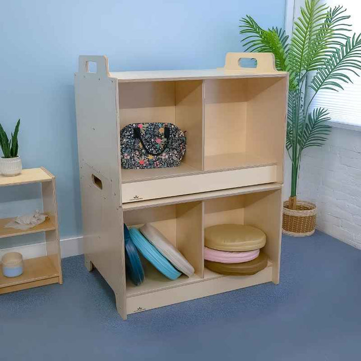 Two Whitney Brothers Stack-Able Tables stacked as a four-compartment storage cabinet in a classroom setting, with floor cushions and balance discs organised in the lower compartments