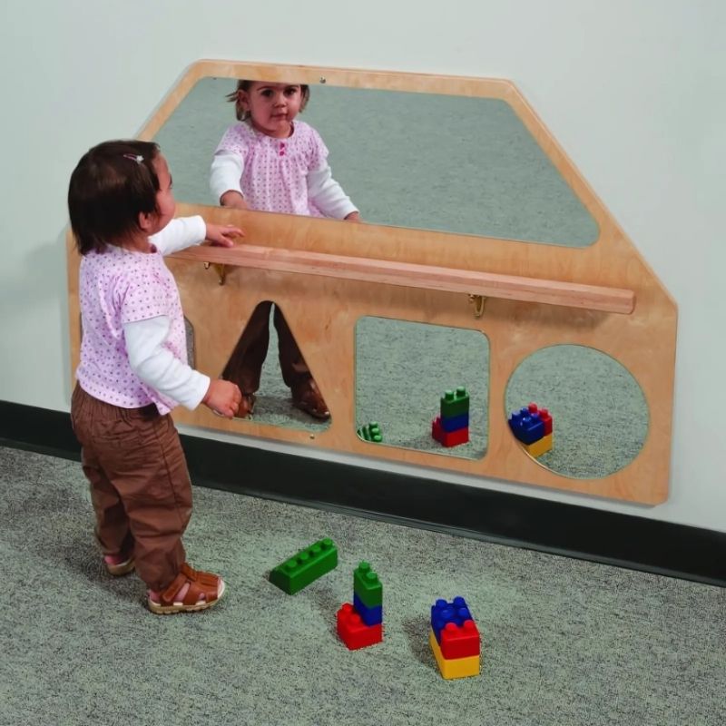 Toddler using the Whitney Brothers Wall Mirrors with Pull Up Bar, gripping the pull-up bar to pull to standing while looking at their reflection in the five shatterproof acrylic mirror shapes
