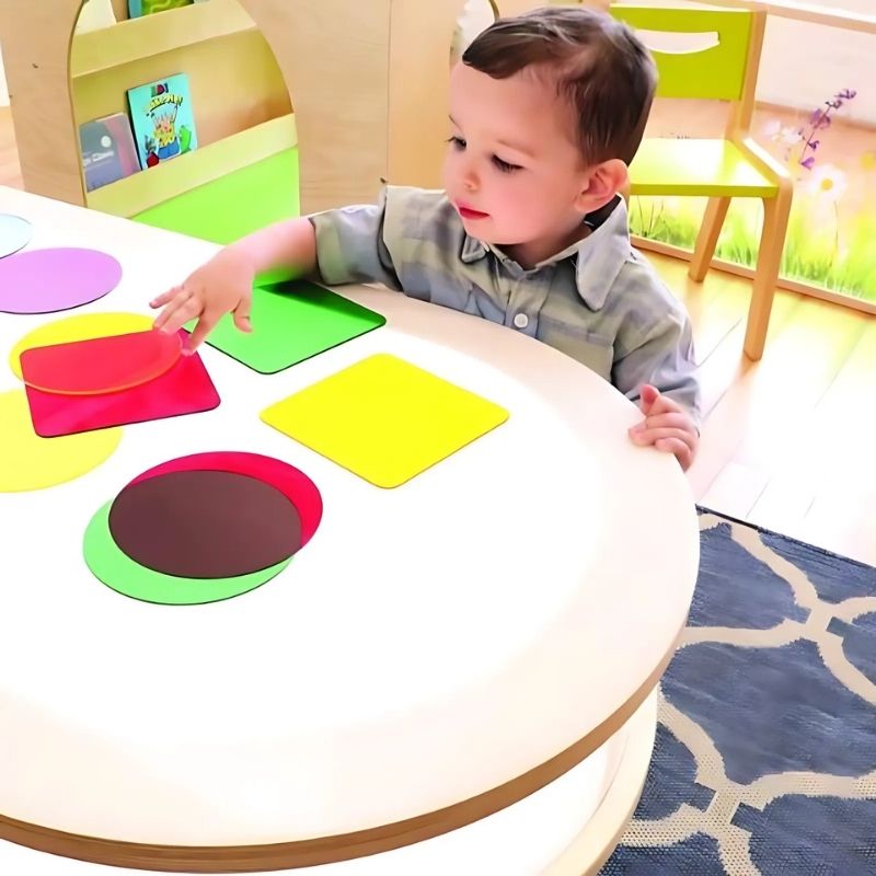 Child playing at the Whitney Brothers Whitney Plus Radiant LED Light Table, exploring translucent materials on the illuminated top surface of the elongated sensory light table