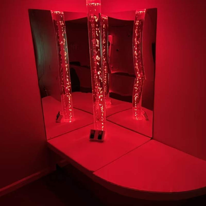 Wide view of a TFH Wireless Bubble Tube in a red-lit mirrored corner sensory room installation