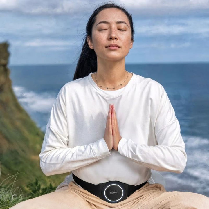 Woman meditating by the ocean with the Woojer Strap 4 worn at the waist, a vibroacoustic wearable for relaxation, breathwork and calm